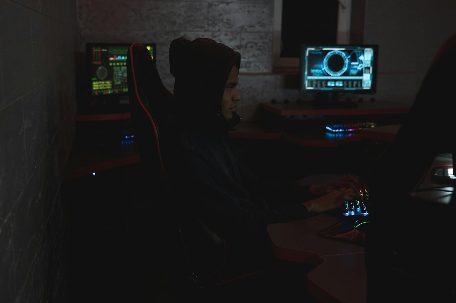 A professional analyzing data on multiple monitors in a dark room, highlighting cybersecurity themes.